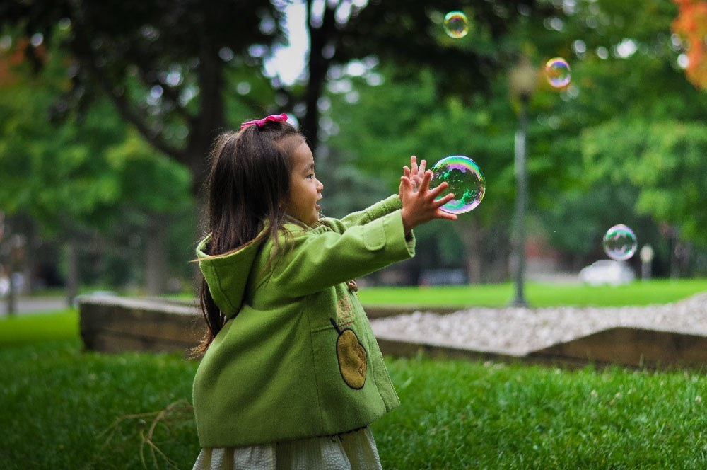 Young girl joyfully reaching for bubbles in a sunlit park